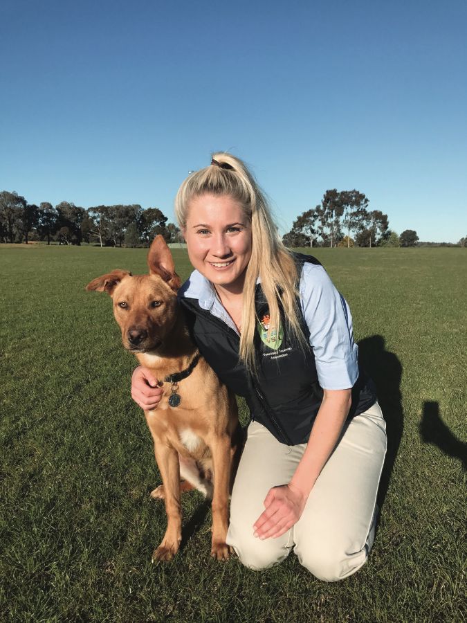 Sammy kneeling in a paddock beside her dog